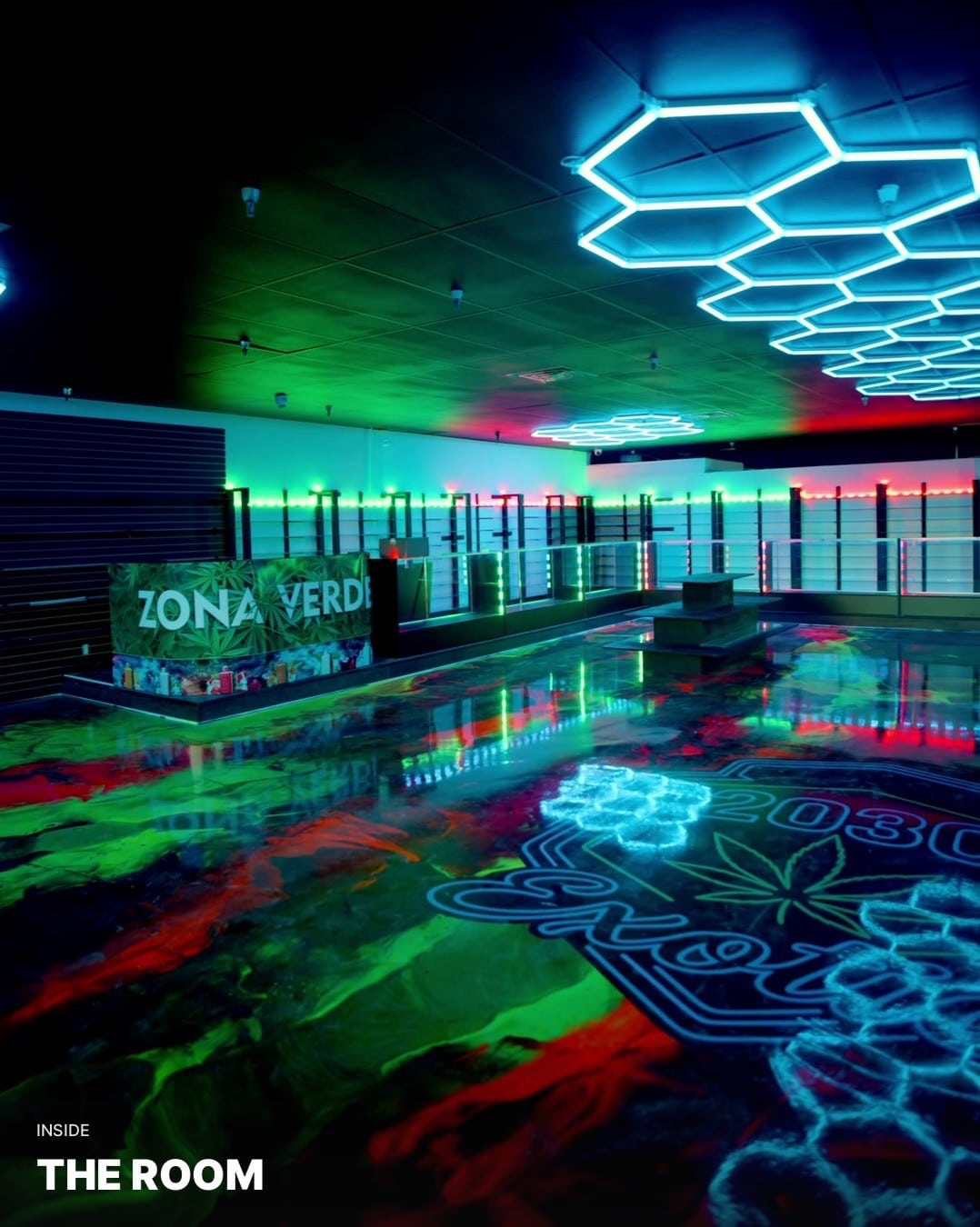 Hexagonal ceiling lights above the colorful floor and display counters inside Zona Verde smoke shop.